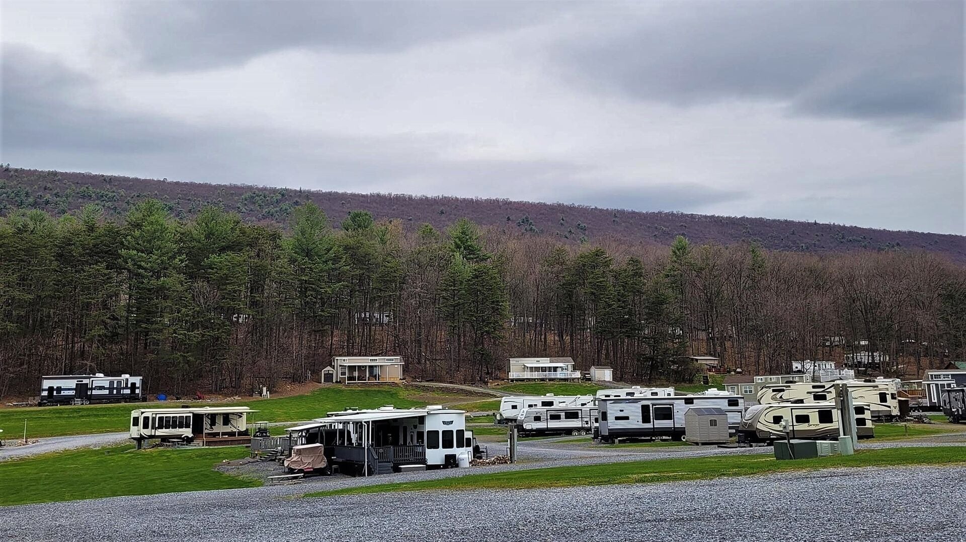 A campground with RVs parked on a gravel area, surrounded by a forested hillside.