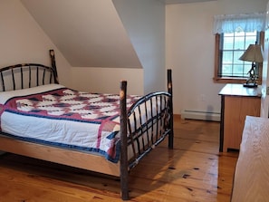 A bedroom with a wooden bed, a quilt, a desk with a lamp, and a window with blinds. - James Creek RV Resort (James Creek)