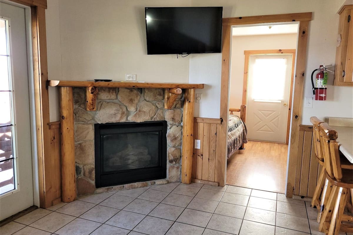 A room with a stone fireplace, a mounted television, and a door leading to another room.