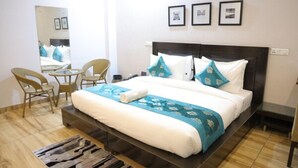Habitación de hotel con cama, una silla, una mesita, un espejo y cuadros en la pared.