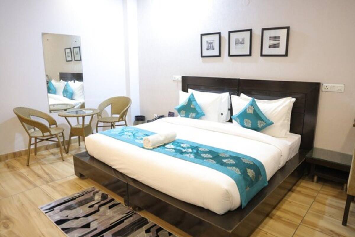 A hotel room with a bed, a chair, a small table, a mirror, and framed pictures on the wall.