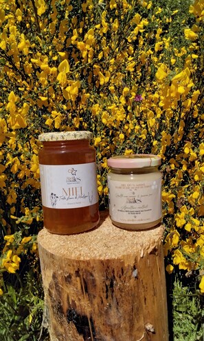 Deux pots de miel posés sur une souche en bois, avec des fleurs jaunes en arriÚre-plan.