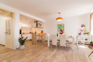A modern kitchen with white cabinets, a dining area with white chairs, and a bright orange pendant light. - Villa Pietra house situated Galižana (Croatia)