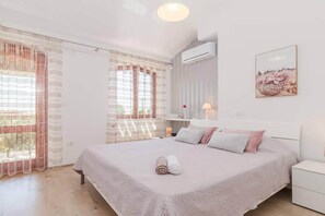 A bedroom with a bed, curtains, an air conditioner, a bedside table, and a wall-mounted picture. - Villa Pietra house situated Galižana (Croatia)