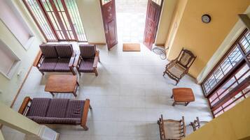 Um quarto amplo com uma grande porta aberta para o exterior, um conjunto de sofás, uma mesa de madeira e uma cadeira de vime.