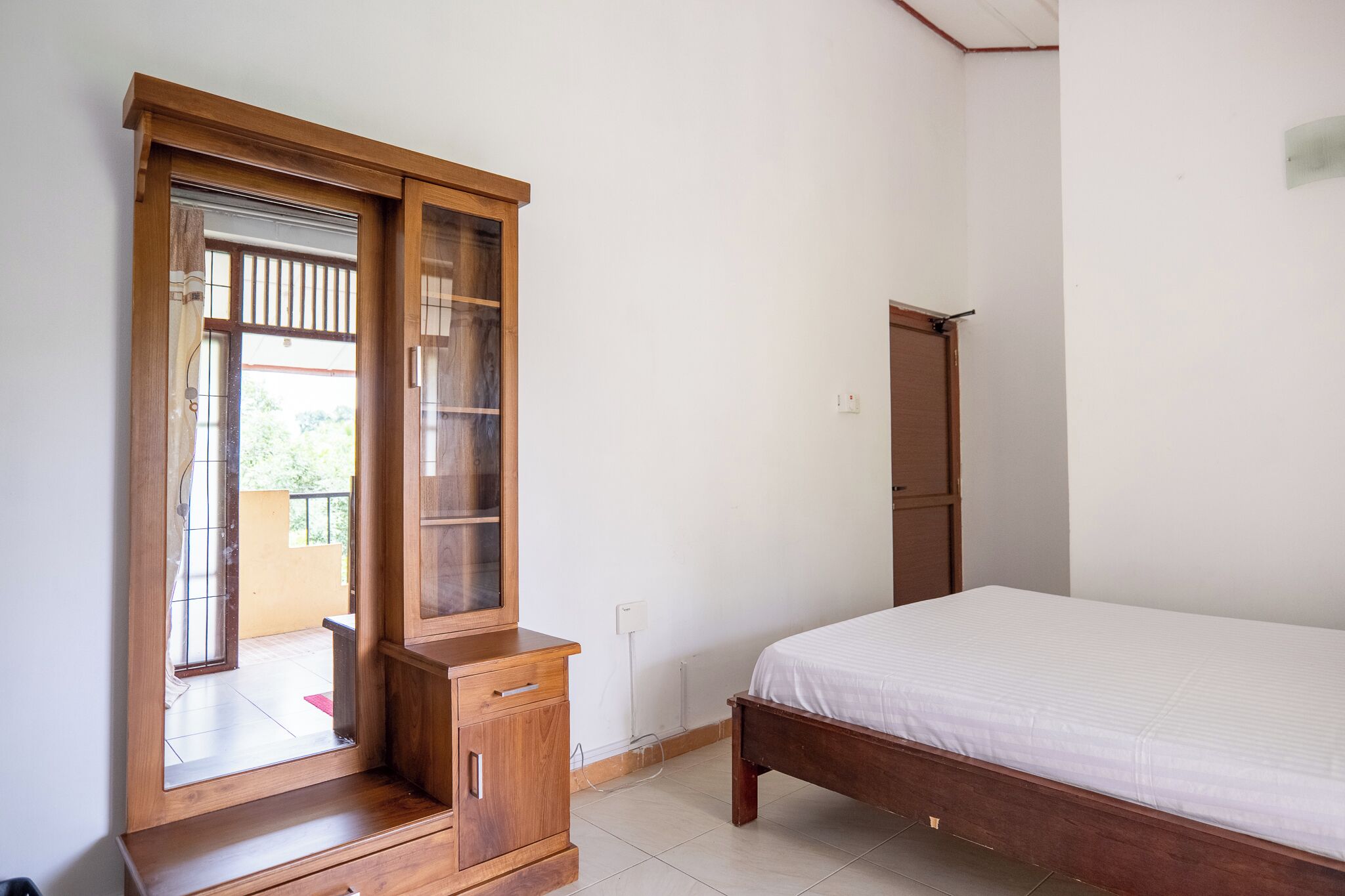 A bedroom with a wooden wardrobe, a bed, and a door.