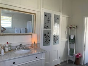 Casa de banho com toucador branco, um espelho grande, uma pia e painéis de vidro decorativos.