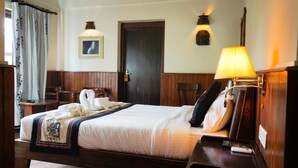 Ein Hotelzimmer mit einem Bett, einem Nachttisch, einer Lampe, einem Sessel, einer Tür und einem Wandbild.