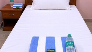 A neatly made bed with a white pillow, a blue and white striped towel, and a bottle of Bisleri water. - Hotel Akshni Palace (Purnia)