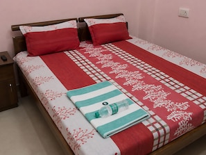 Una cama bien tendida con una colcha de cuadros rojos y blancos, dos almohadas rojas y una toalla doblada con un borde verde.
