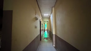 Un couloir étroit, éclairé par un puits de lumière, et une pièce illuminée de lumière verte au bout.