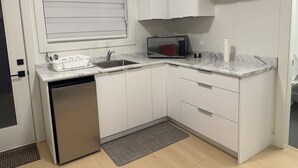 A compact kitchen with white cabinets, a dishwasher, a microwave, and a marble countertop. - Feel Home out of home (Abbotsford)
