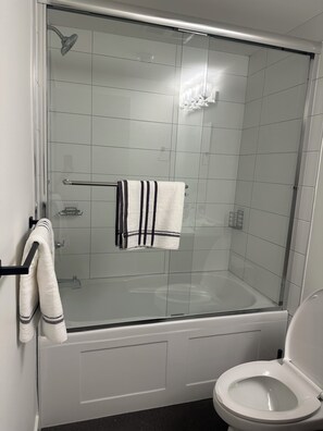 A bathroom with a glass-enclosed shower, a white toilet, and a towel rack with towels. - Feel Home out of home (Abbotsford)
