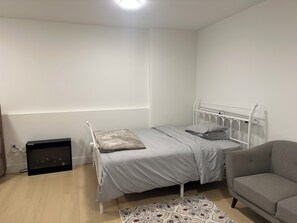 A bedroom with a bed, a chair, a rug, and a small cabinet. - Feel Home out of home (Abbotsford)