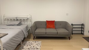 A bedroom with a bed, a grey sofa, a patterned rug, and a black metal rack. - Feel Home out of home (Abbotsford)