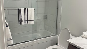 A modern bathroom with a glass-enclosed shower, a toilet, and a vanity with a marble countertop. - Feel Home out of home (Abbotsford)