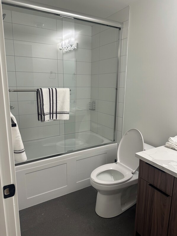 A modern bathroom with a glass-enclosed shower, a toilet, and a vanity with a marble countertop.