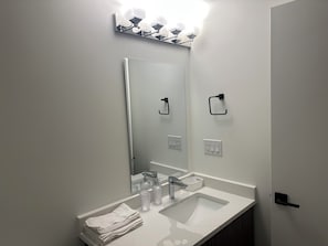 Un baño con lavamanos, espejo, toallero e iluminación.