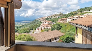 Blick von einem Balkon auf eine Hügelstadt mit terrakottafarbenen Dächern und üppiger Vegetation.