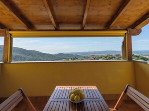 A balcony with a wooden table and chairs, a bowl of lemons, and a scenic view of hills and buildings. - Bellavista by Interhome (Scarlino)