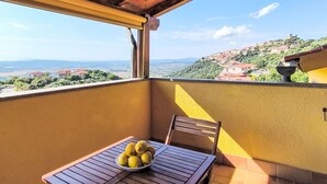 Ein Balkon mit Tisch und einer Zitronenschale, mit Blick auf einen Hügel mit Gebäuden.