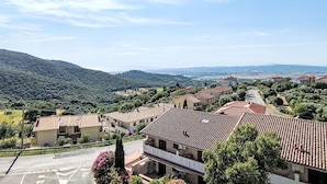 Ein Wohngebiet mit Häusern mit Terrakotta-Dächern, einem wolkenlosen Himmel und einer hügeligen Landschaft im Hintergrund.