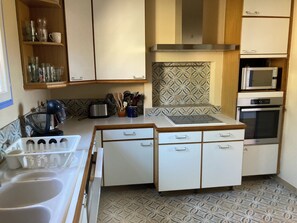 A compact kitchen with white cabinets, a microwave, an oven, and a patterned backsplash. - House sea view private pool (Bormes-les-Mimosas)