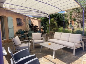An outdoor patio with a covered seating area, stone flooring, and surrounding greenery. - House sea view private pool (Bormes-les-Mimosas)