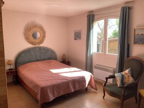 A bedroom with a bed, a chair, a mirror, a window with curtains, a radiator, and a small table with a lamp. - House sea view private pool (Bormes-les-Mimosas)