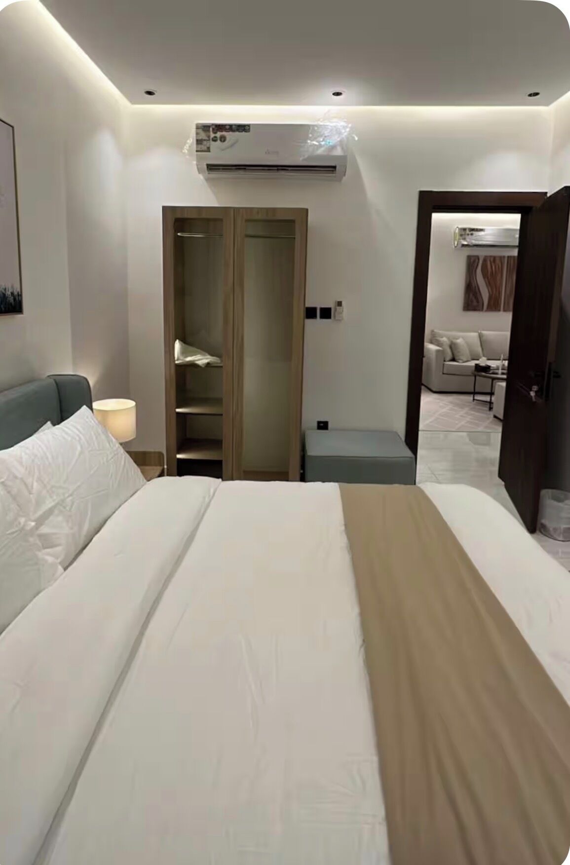 A hotel room with a bed, a wardrobe, a desk, and an air conditioning unit.