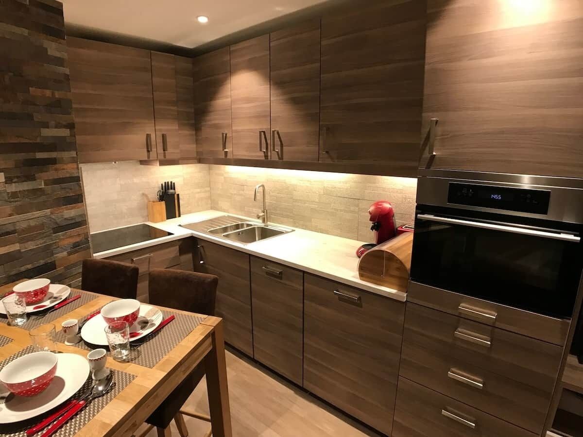 Une cuisine moderne avec des meubles en bois, un four en acier inoxydable et un coin repas aménagé pour quatre personnes.