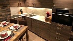 A modern kitchen with wooden cabinets, a stainless steel oven, and a dining area set for four. - Studio "Le Chamois" in Tignes Val Claret (Tignes)