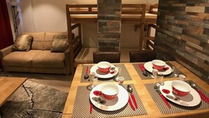 A dining area with a wooden table set for four, a sofa, and a stone accent wall. - Studio "Le Chamois" in Tignes Val Claret (Tignes)