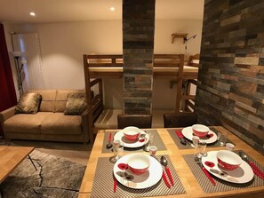 Ein Essbereich mit Holztisch, gedeckt für vier Personen, einer Couch und einer Wand aus Naturstein.