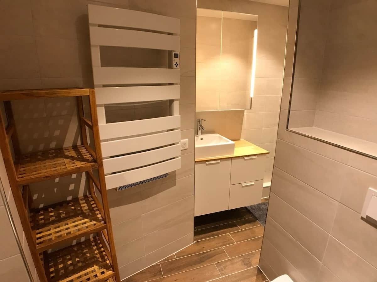 A bathroom with a white sink, a mirror, and a wooden shelf unit.