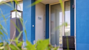 Ein blaues Gebäude mit Glastür, einem Schild, das es als Apartment kennzeichnet, und einer kleinen Außenbereich-Sitzgelegenheit.