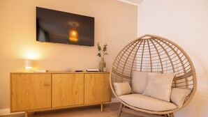 Ein Zimmer mit einem Holzschrank, einem an der Wand befestigten Fernseher und einem Korbstuhl mit Kissen.