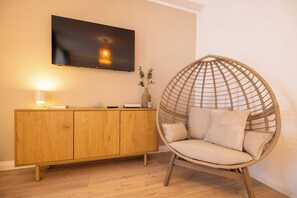 Huoneessa on puinen kaappi, seinälle asennettu televisio ja rottinkituoli, jossa on pehmusteet.