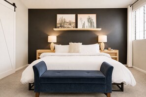 Ein Schlafzimmer mit einem Bett, Nachttischen, Lampen, einer Bank und zwei an der Wand befestigten Bildern.
