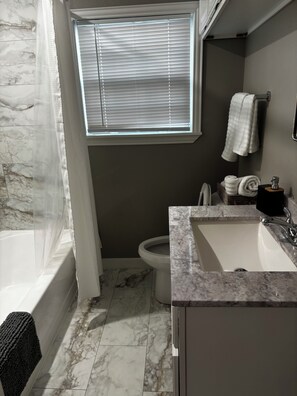 Ein Badezimmer mit Badewanne, Toilette, Waschbecken und einem Fenster mit Jalousien.