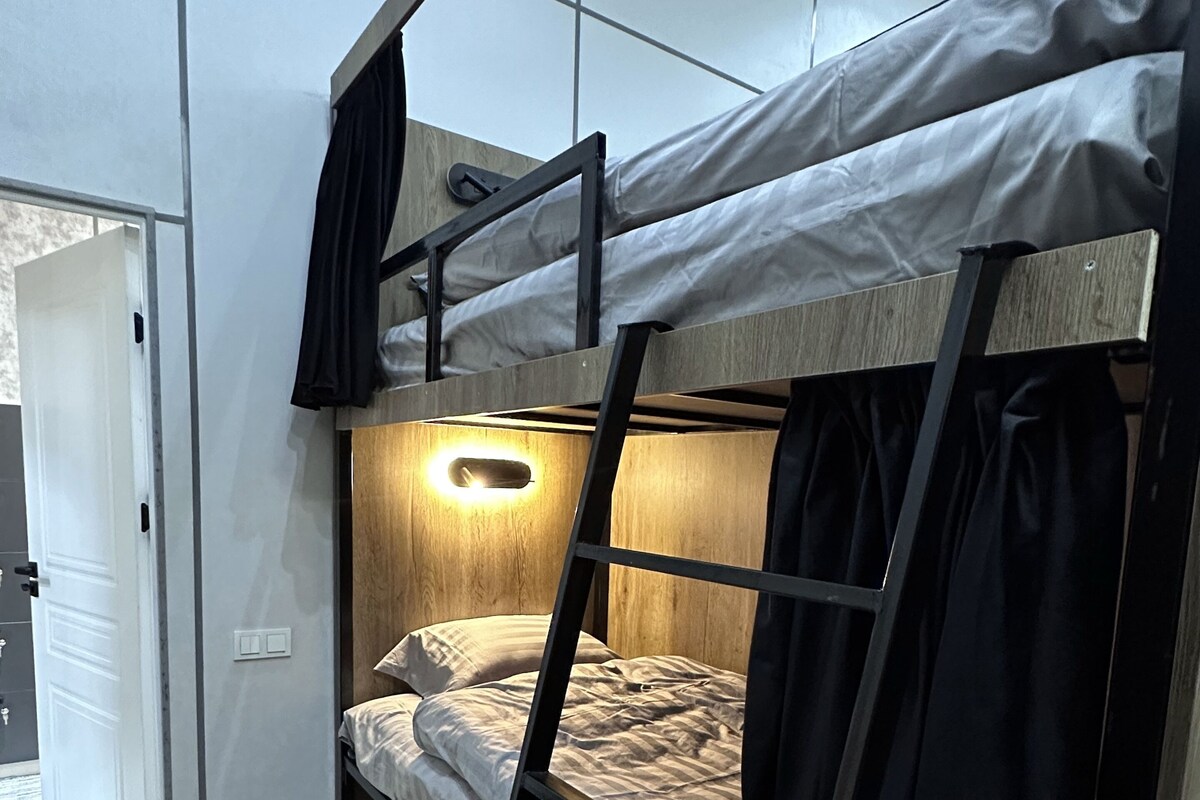 A bunk bed with a ladder, a bedside lamp, and a door leading to another room.