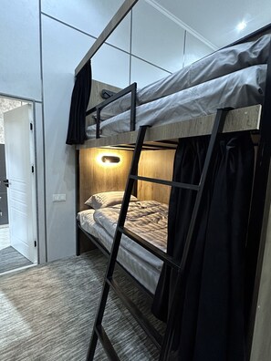 Una cama litera con escalera, una lámpara de noche y una puerta que da a otra habitación.