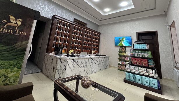 Una zona de recepción con mostrador de mármol, una pared con exhibición de tés y una pantalla de televisión.