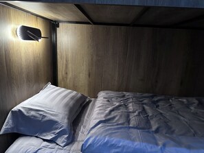 A bunk bed with a headboard, a bedside lamp, and a wooden wall.