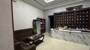 Un hall con un sofá, una mesa de centro, un mostrador de recepción, una exhibición de tés y una pared con estanterías.