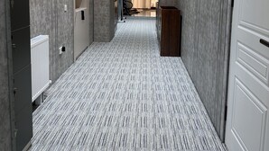 Un pasillo con alfombra estampada, un radiador, una puerta blanca y un escritorio de madera.