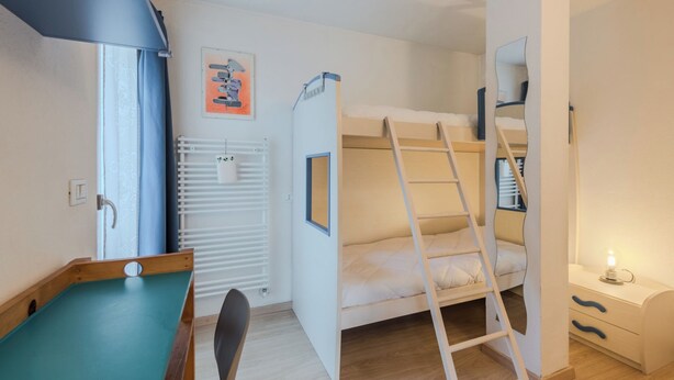 Een slaapkamer met stapelbed, bureau, stoel en radiator.