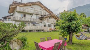 Een chalet met twee verdiepingen, een balkon, een eethoek met tafel en stoelen, en een hangmat.
