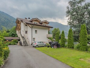 A two-story building with a staircase leading to the entrance, a parked car, and a motorcycle covered with a tarp. - Casa Roby by Interhome (Pinzolo)