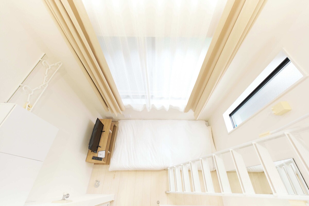 Een kamer met een dakraam, een klein raam, een wit wiegje en een houten kast.